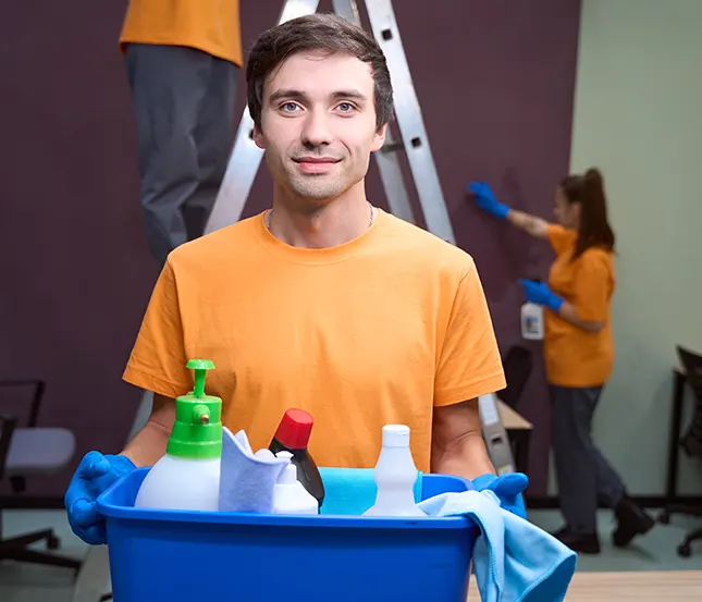 A friendly Choice Cleaning Plus worker holding a caddy of cleaning supplies