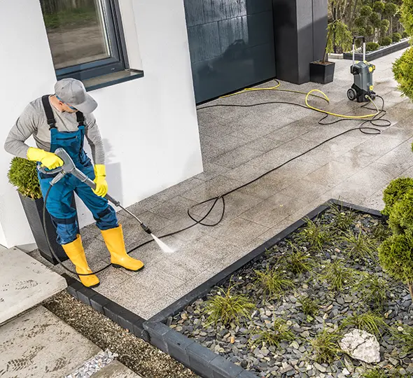 A Choice Cleaning Plus technician pressure washing concrete beside a modern home