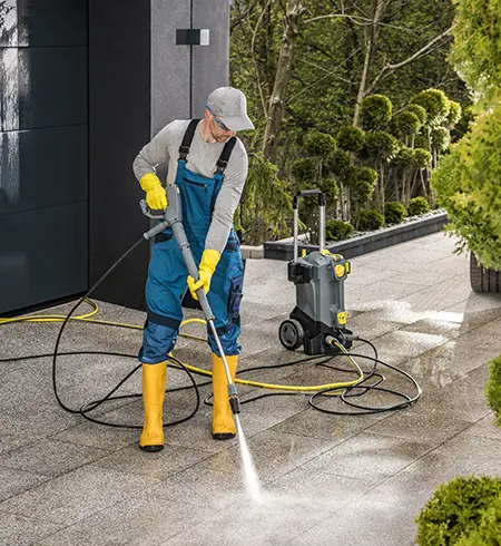 A technician pressure washing a curved concrete walkway with a surface cleaner