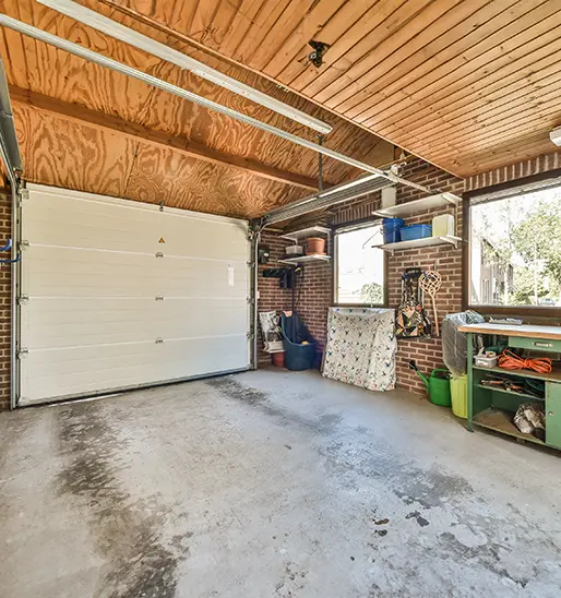 A homeowner on a ladder cleaning the exterior trim of a garage with a red car parked inside