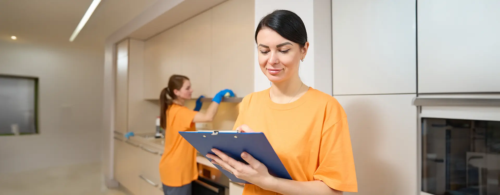 A Choice Cleaning Plus team member reviewing a checklist while a colleague cleans a kitchen