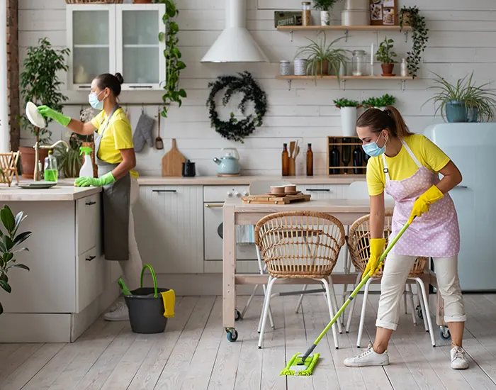 Two professional cleaners in masks wiping surfaces and mopping a modern kitchen
