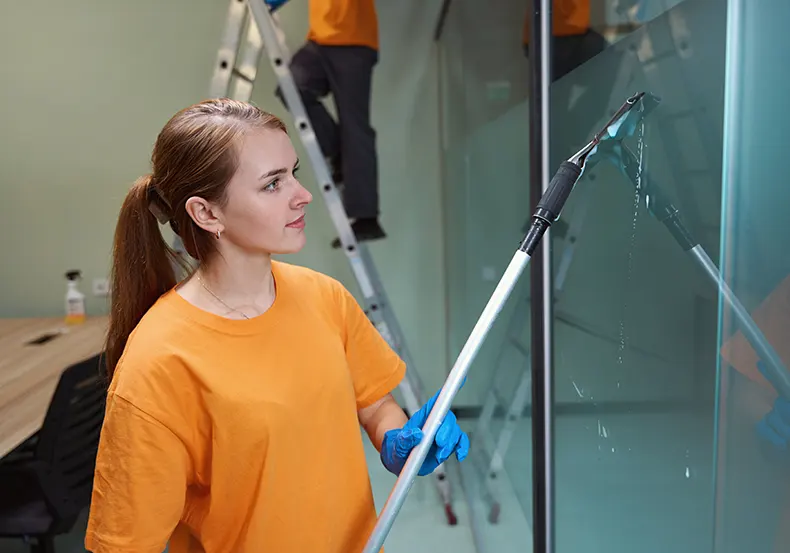 A Choice Cleaning Plus janitor cleaning a tall glass partition after construction